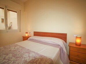 Ein Schlafzimmer mit einem Bett, einem Nachttisch, einer Lampe und einem Fenster.