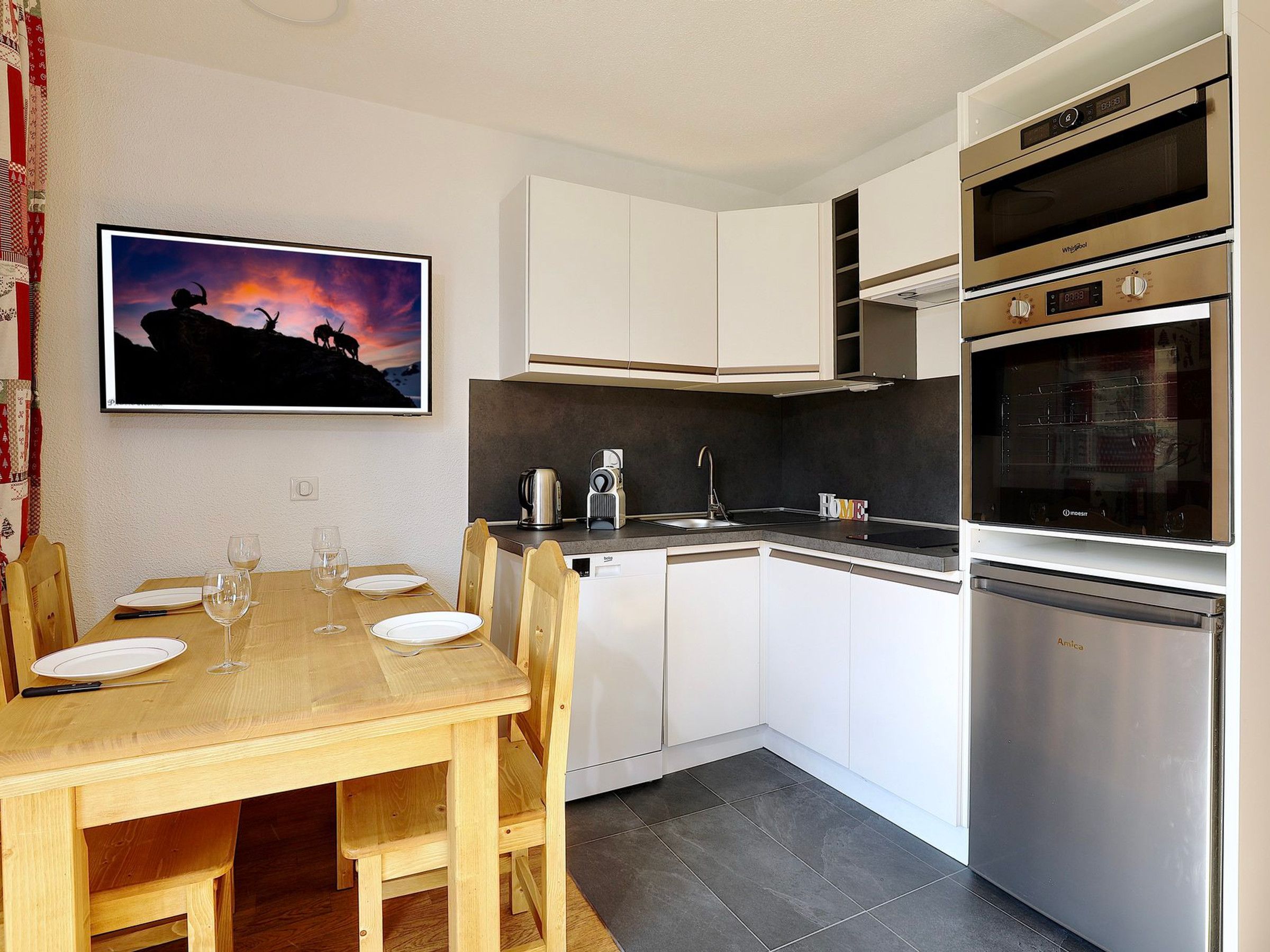 A modern kitchen with white cabinets, a wooden dining table, and a built-in oven.
