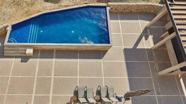 A swimming pool with a tiled deck, a set of sun loungers, and a wooden pergola structure.
