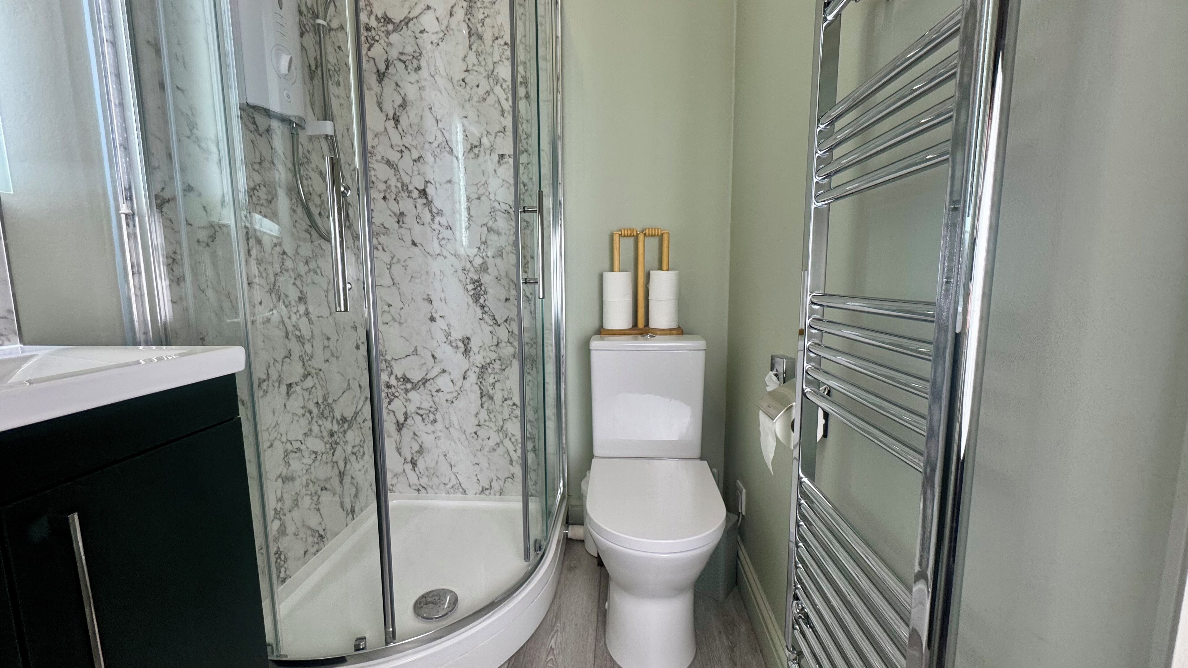 Ein Badezimmer mit einer gläsernen Duschkabine, einer weißen Toilette und einem chromfarbenen Handtuchhalter.