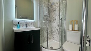 A bathroom with a glass-enclosed shower, a sink with a marble backsplash, and a toilet. - The Cricketers Inn (Winchester)