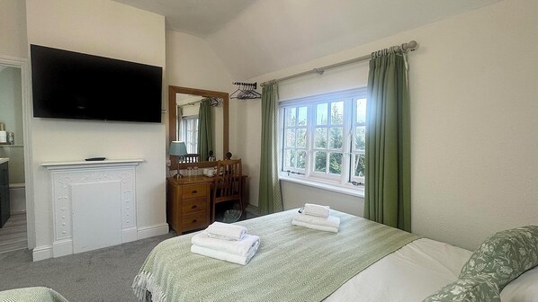 A bedroom with a bed, a dresser, a mirror, a television, and a window with curtains.