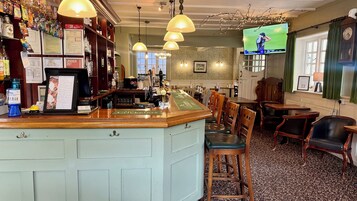 Zona de bar con mostrador, sillas de madera y un televisor mostrando un evento deportivo.