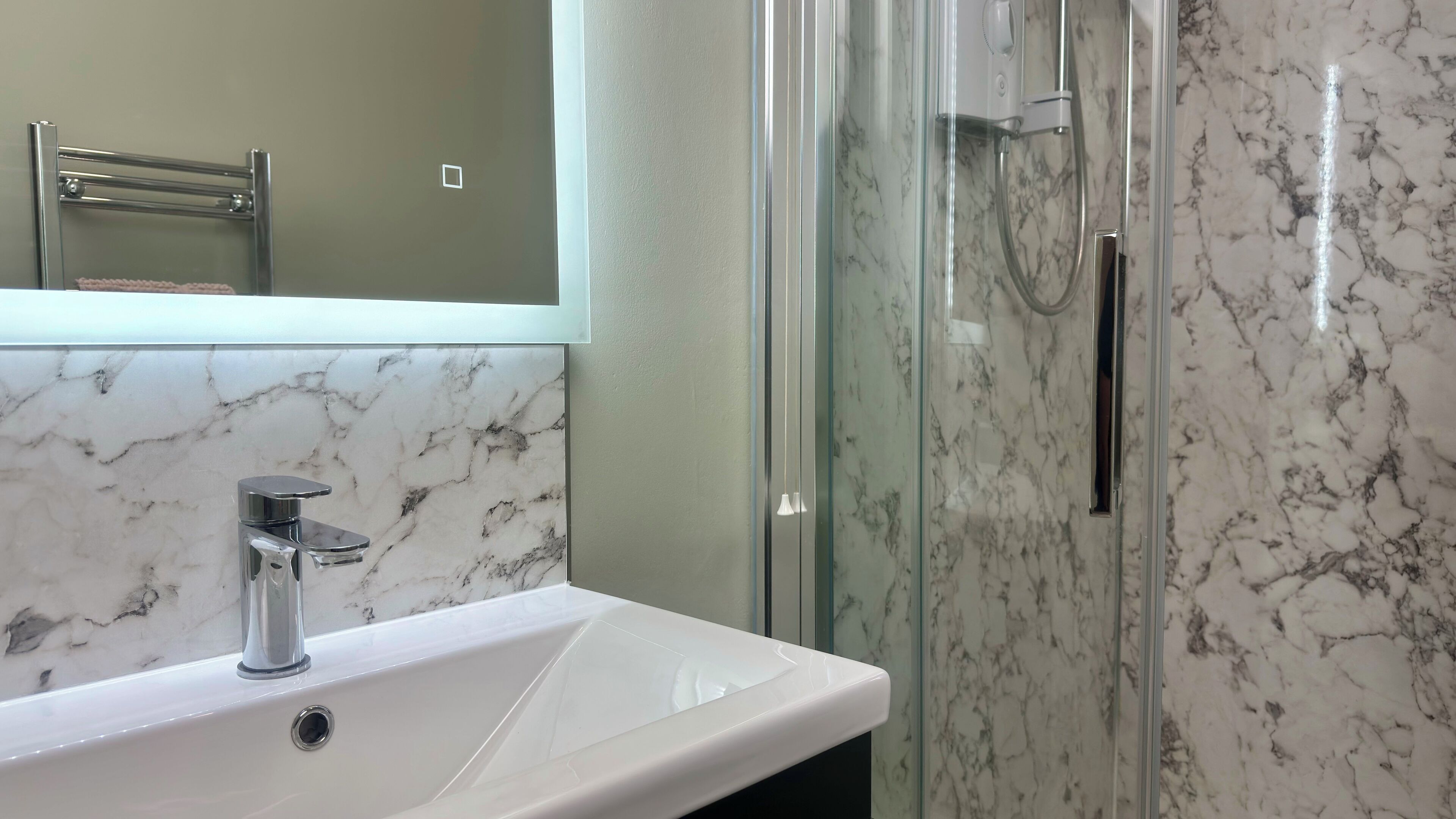 A bathroom with a white sink, a glass shower enclosure, and a marble backsplash.