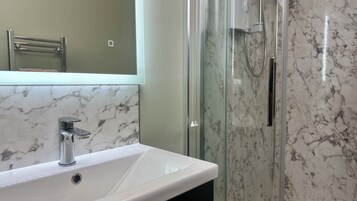 A bathroom with a white sink, a glass shower enclosure, and a marble backsplash.