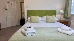A hotel room with a bed, pillows, a nightstand, a lamp, and a window with curtains. - The Cricketers Inn (Winchester)
