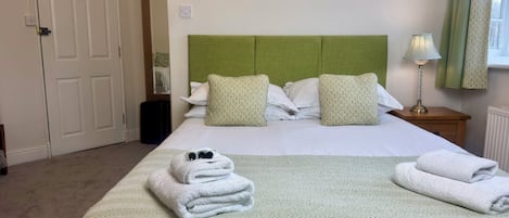 Habitación de hotel con cama, almohadas, mesita de noche, lámpara y ventana con cortinas.