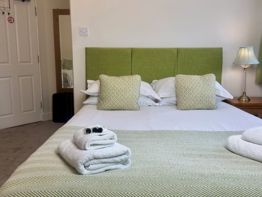 A hotel room with a bed, pillows, a nightstand, a lamp, and a window with curtains.
