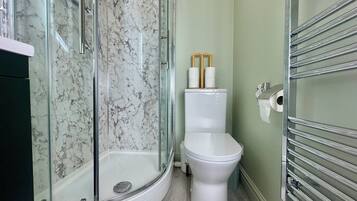 Un baño con cabina de ducha de vidrio, inodoro y dispensador de toallas de papel.