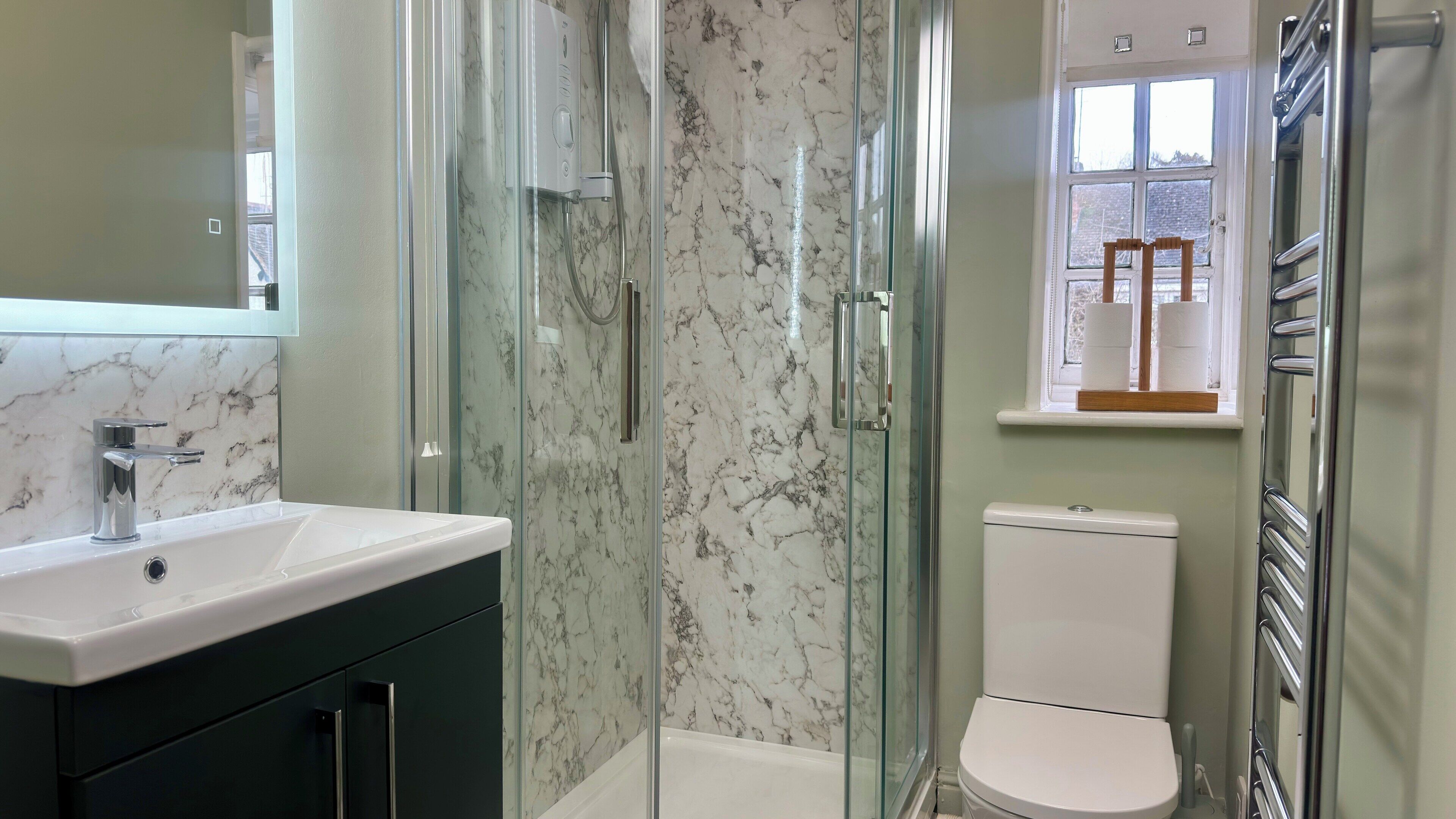 A bathroom with a glass-enclosed shower, a white toilet, and a sink with a marble countertop.