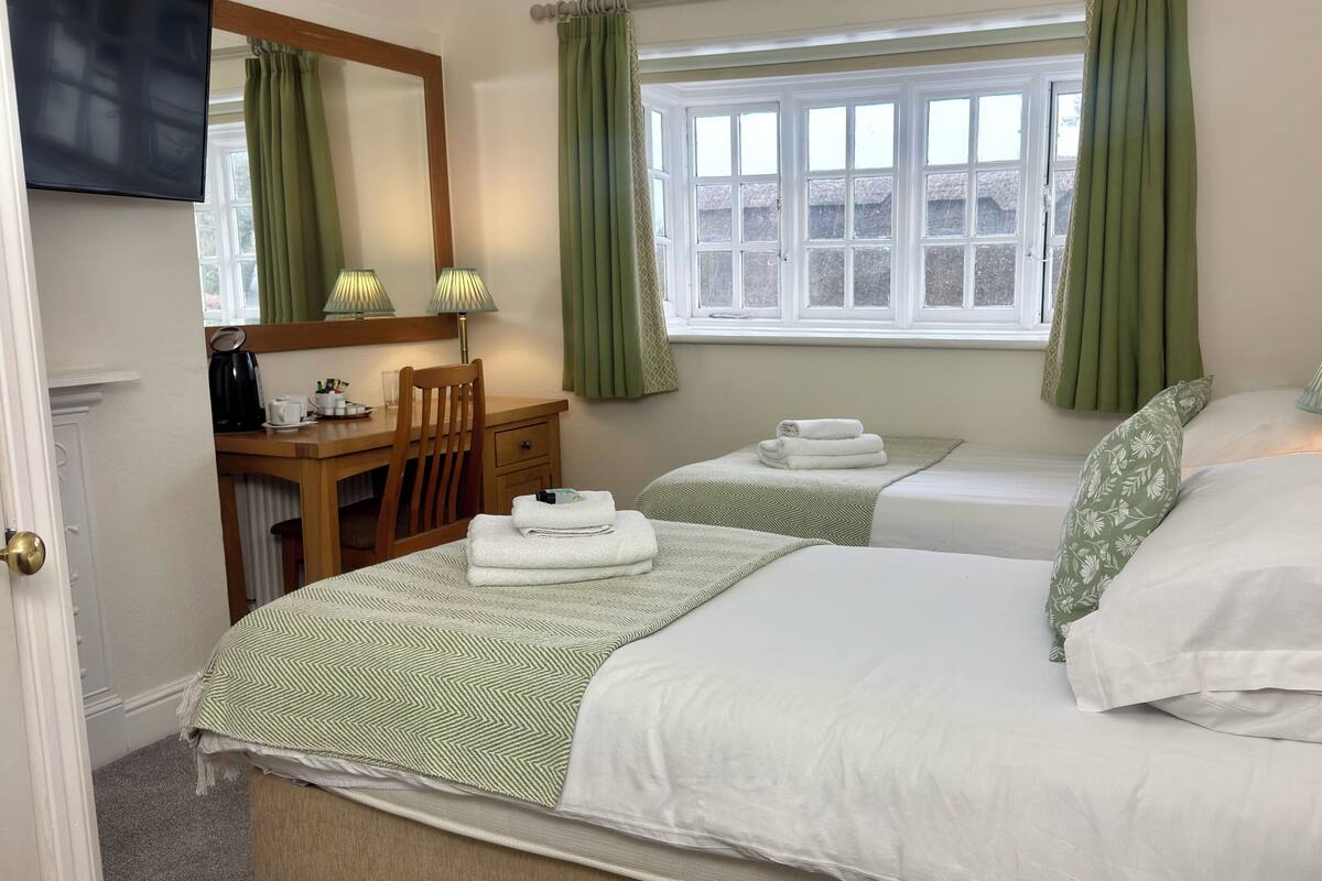 A hotel room with two beds, a desk, a chair, a TV, and a window with curtains.
