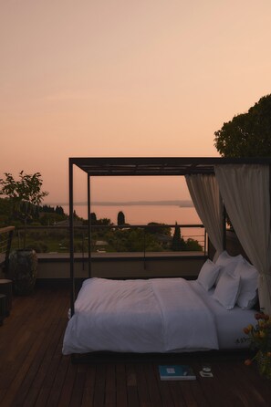 A bedroom with a canopy bed, a view of the landscape, and a book on the nightstand. - Cape of Senses (Torri del Benaco)