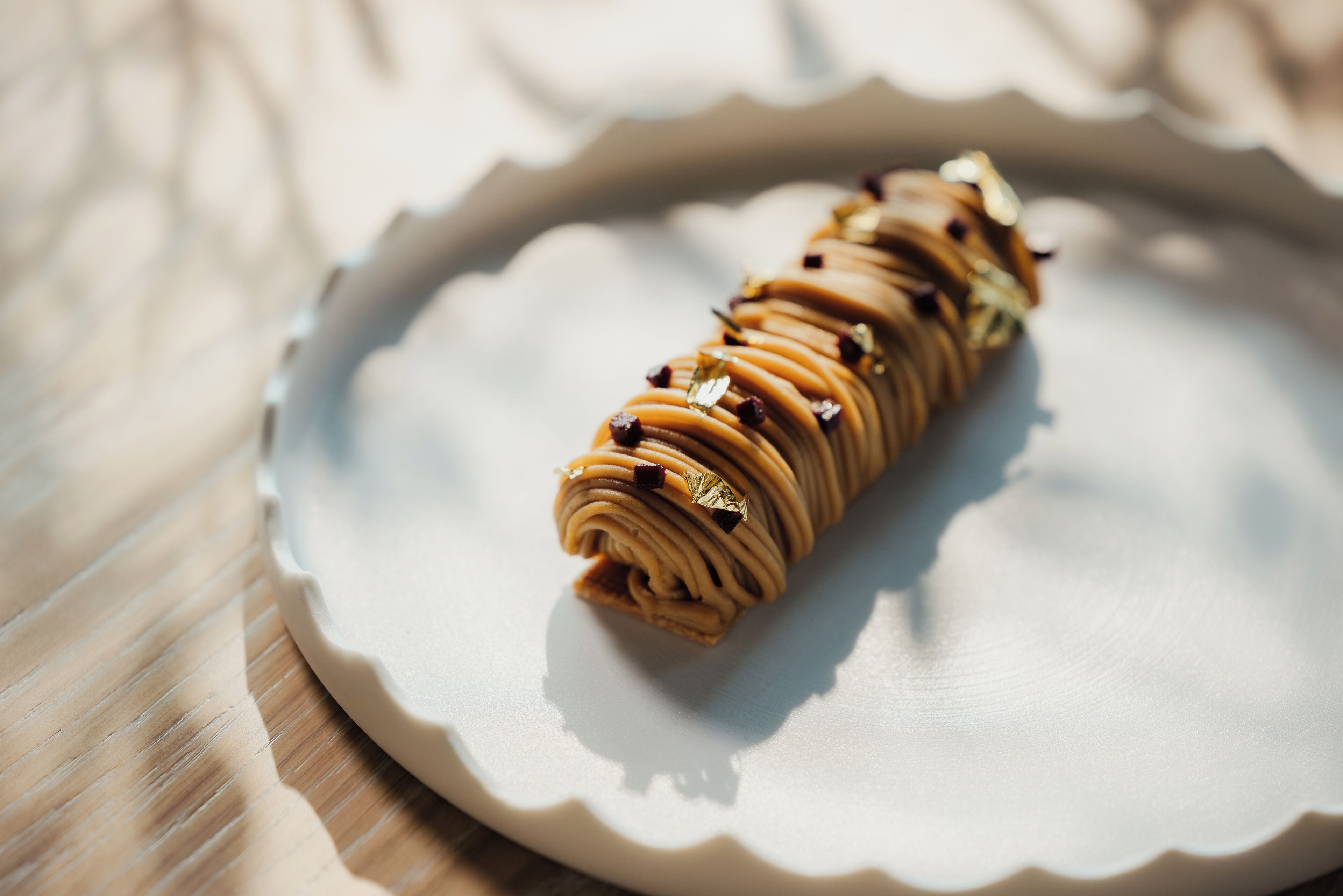 Une pâtisserie enroulée, présentée sur une assiette blanche à bords festonnés, posée sur une surface en bois.