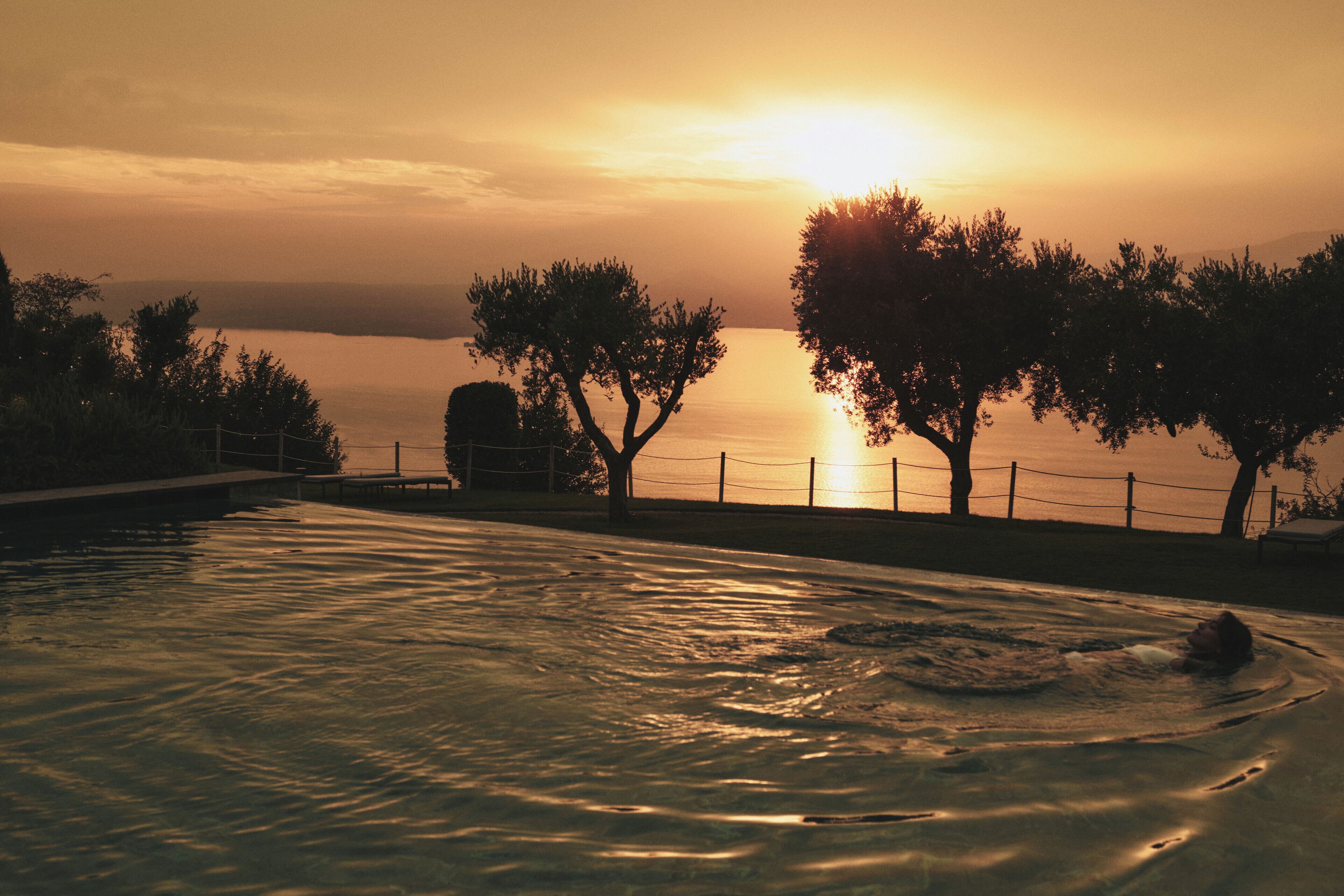 A swimming pool with a sunset view, trees, and a fence.