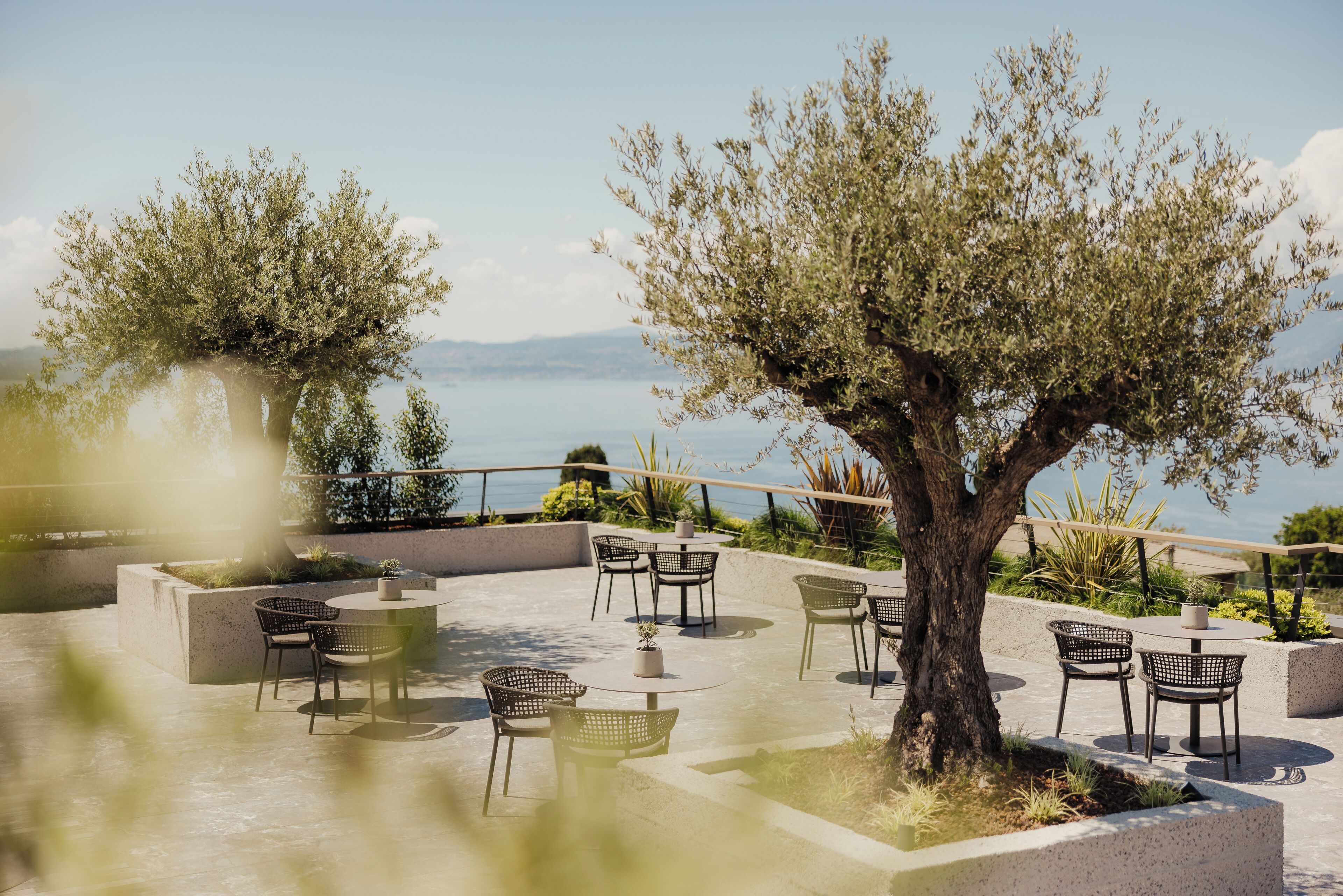 Un espace extérieur aménagé avec des tables et des chaises, entouré de verdure et offrant une vue sur une étendue d’eau.