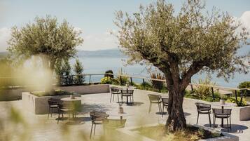 Un espace extérieur aménagé avec des tables et des chaises, entouré de verdure et offrant une vue sur une étendue d’eau.