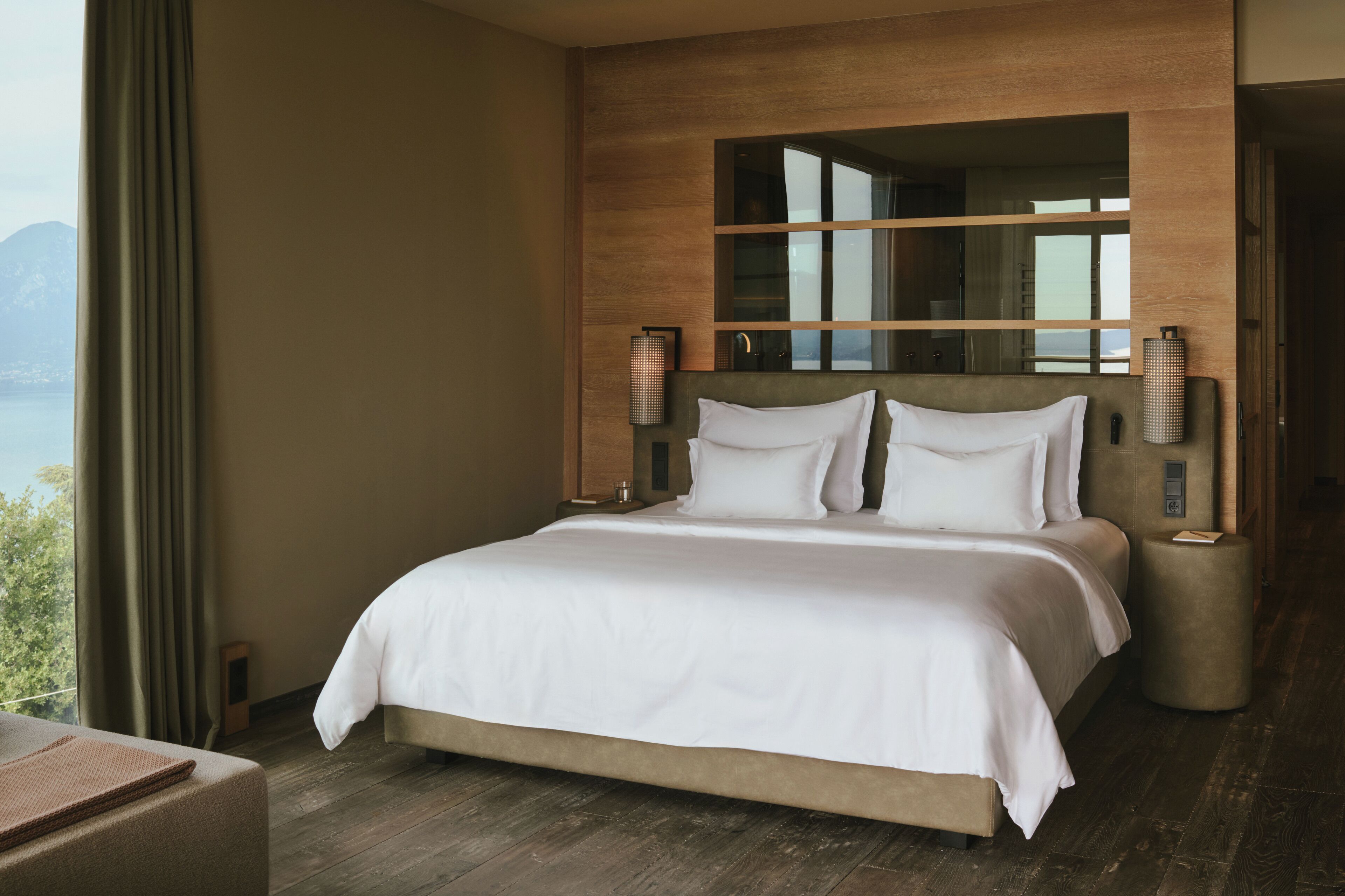 Una habitación de hotel moderna con una cama grande, cabecera de madera y vistas a las montañas.