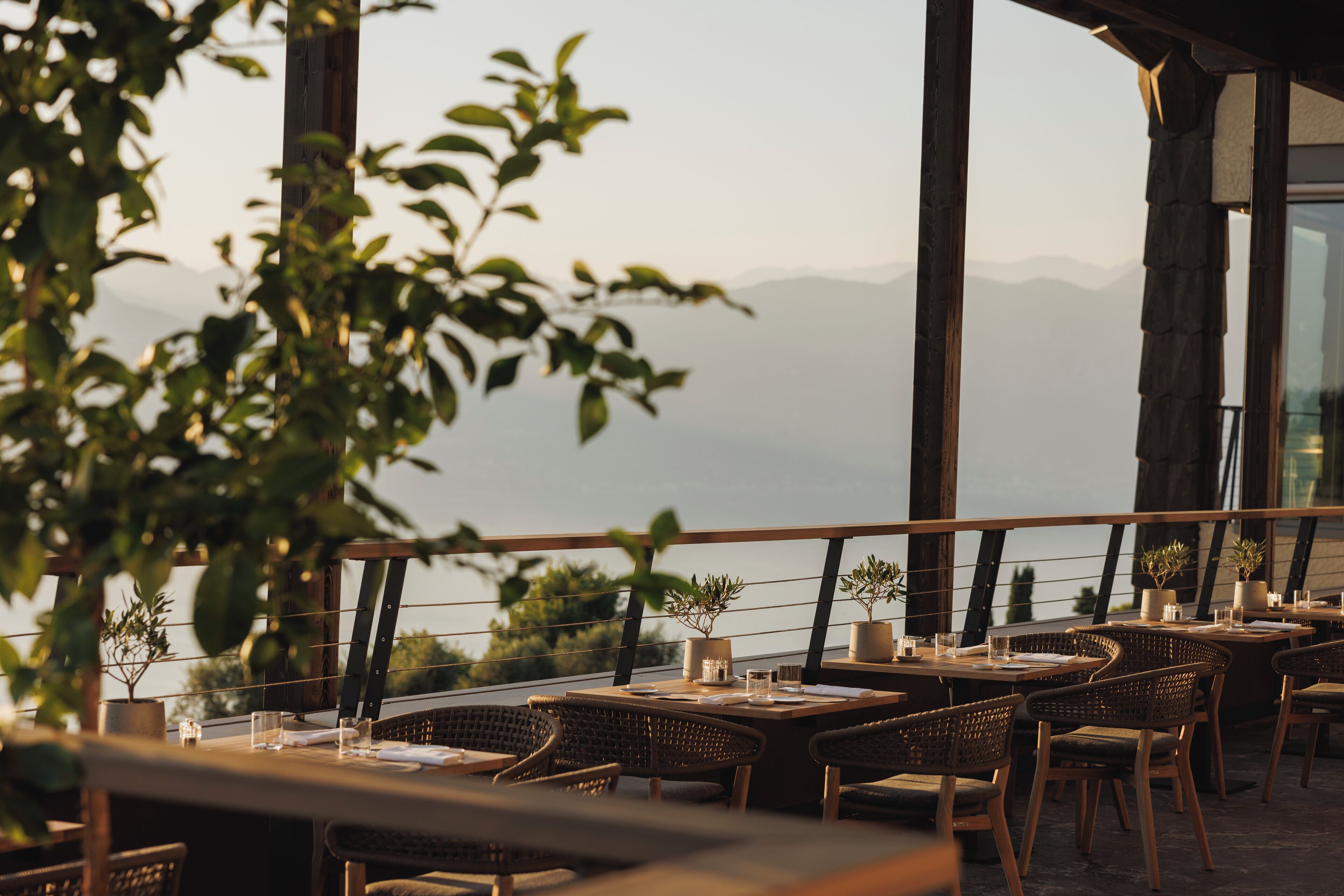 An outdoor dining area with tables and wicker chairs, overlooking a mountainous landscape.