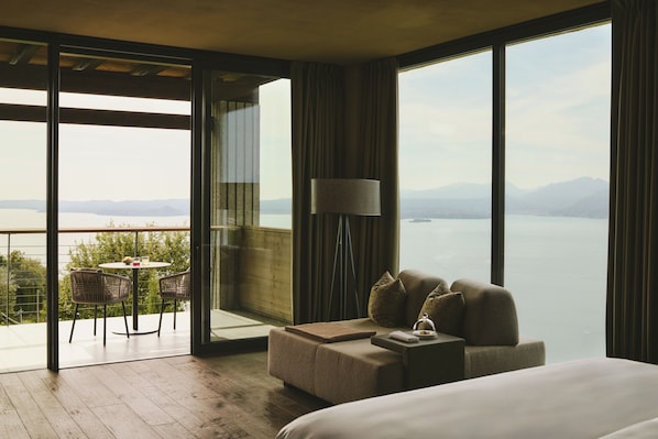 A hotel room with a large window, a sofa, a table with chairs, and a lamp. - Cape of Senses (Torri del Benaco)