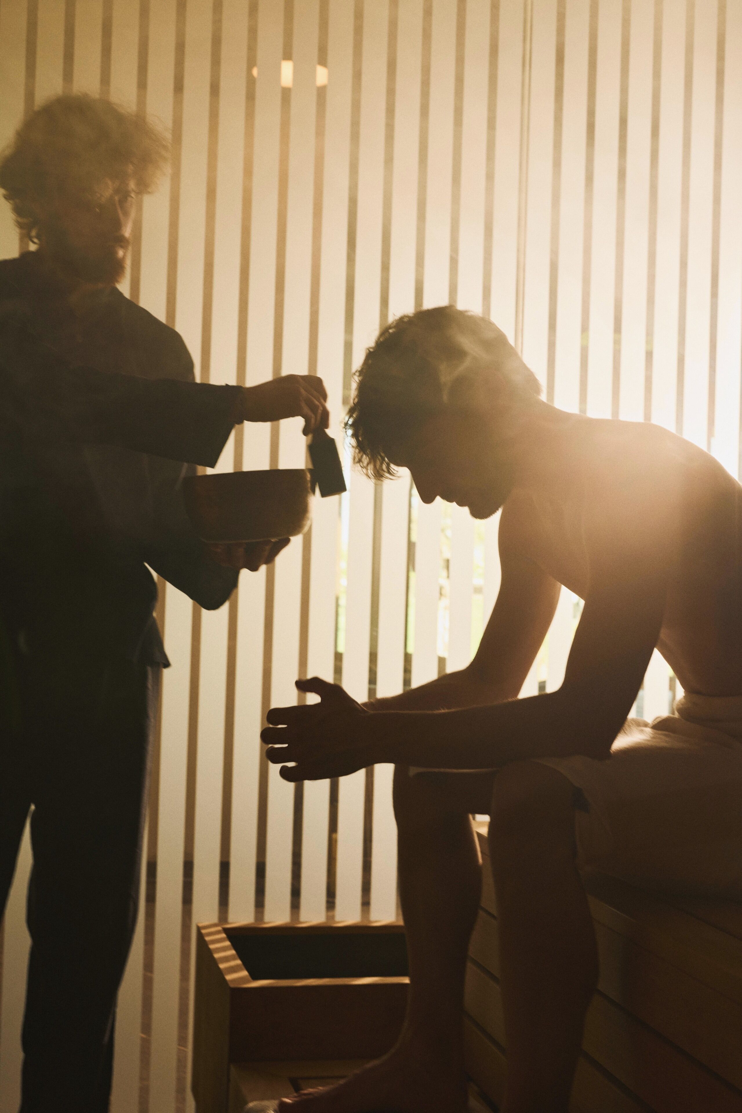 A person sitting on a bench in a room with vertical blinds.