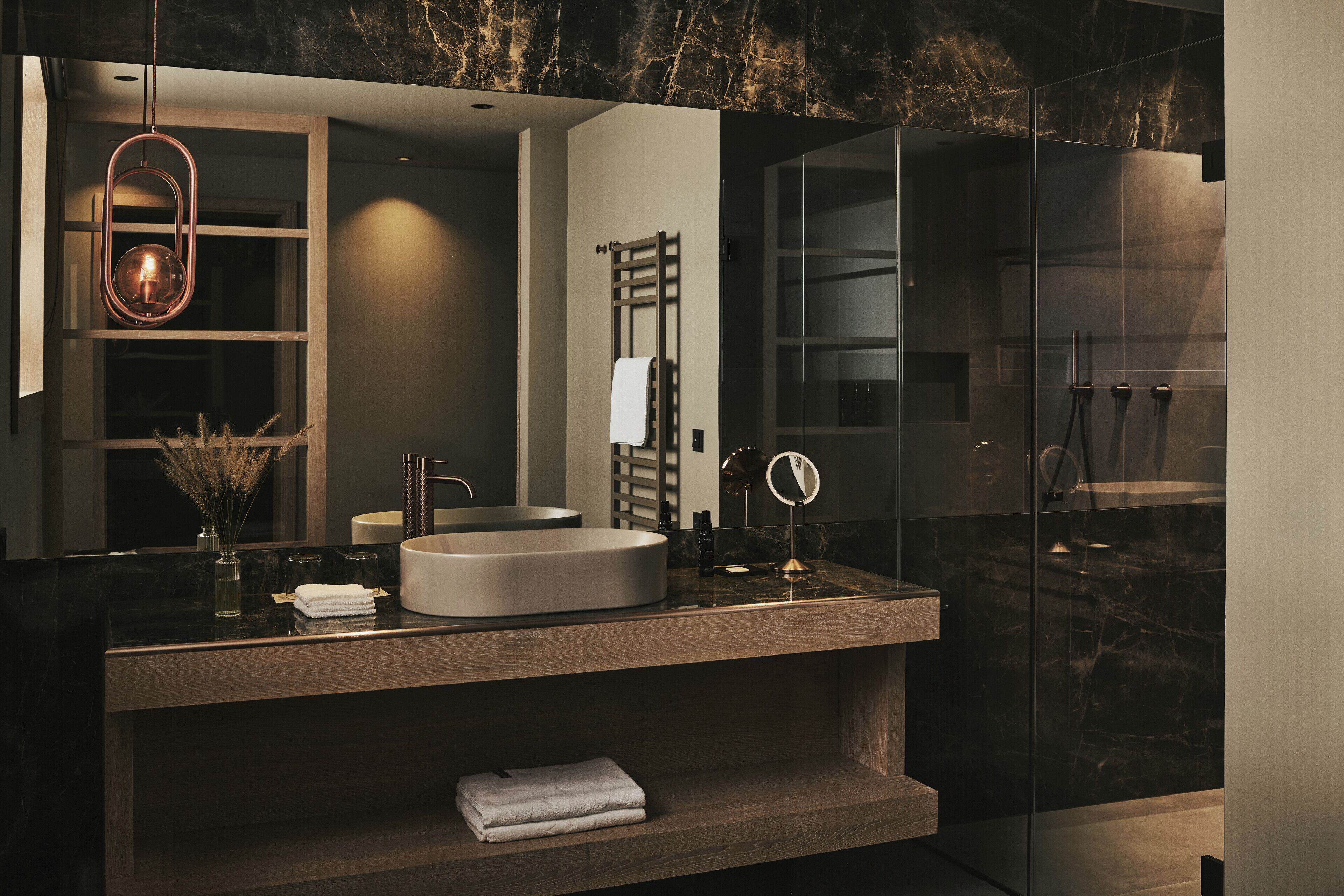 Une salle de bain moderne avec un grand miroir, un lavabo rond et une douche séparée par une paroi de verre.