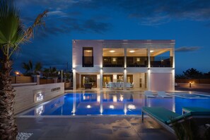A modern two-story hotel with a swimming pool, outdoor seating, and a well-lit entrance. - The ultimate high-class villa with swimming pool (Vir)