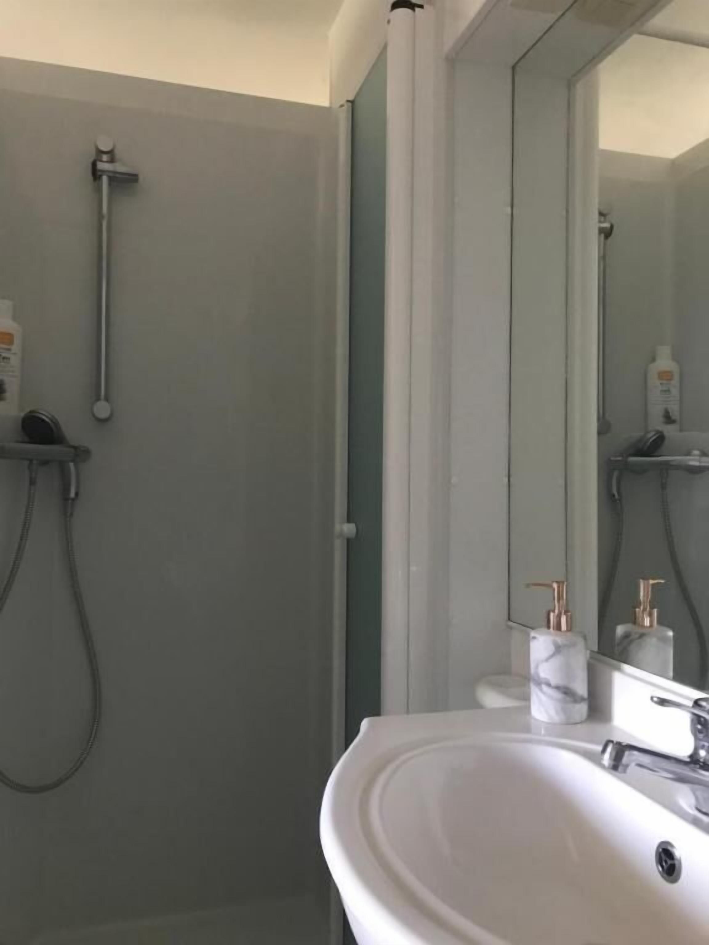 Casa de banho com uma pia branca, espelho e zona de duche.