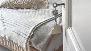 Una cama bien hecha con cabecera, una mesita de noche y una lámpara de pared.