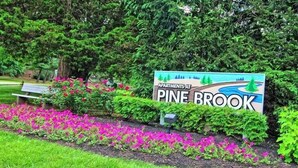 Señal de Pine Brook Apartments con un jardín ajardinado al frente.