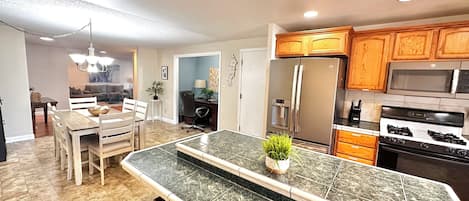 A modern kitchen with a marble island, stainless steel appliances, wooden cabinets, and a dining area with a chandelier.