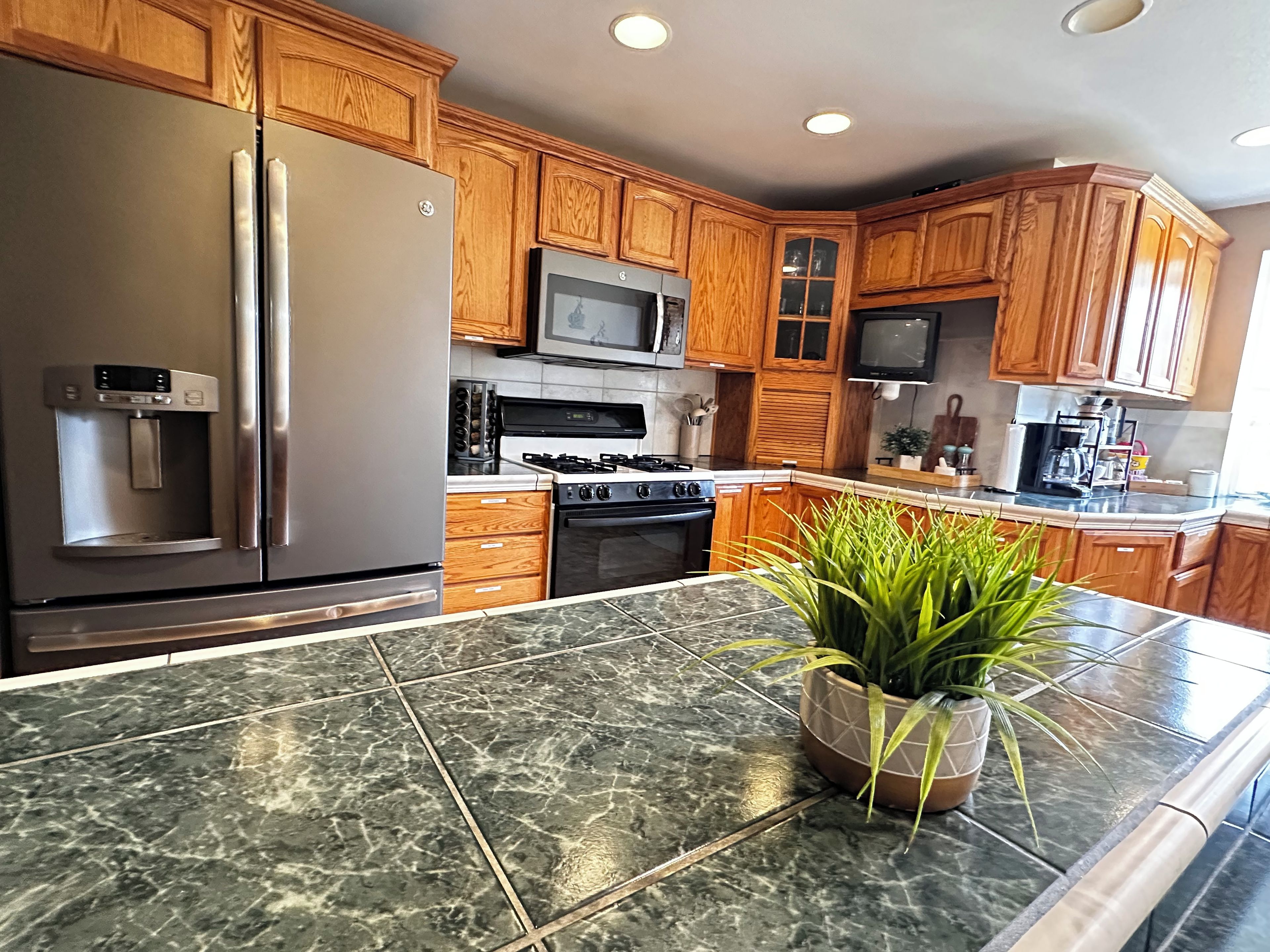 A kitchen with wooden cabinets, stainless steel appliances, a water dispenser, and a potted plant on the countertop.