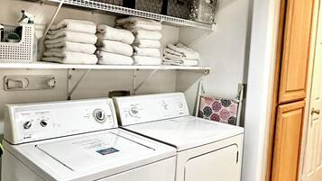 A laundry room with a stacked washer and dryer, shelves with folded towels, and a door to another room.