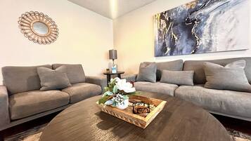 A living room with two grey sofas, a round coffee table with a decorative tray, a wall mirror, and a large abstract painting.