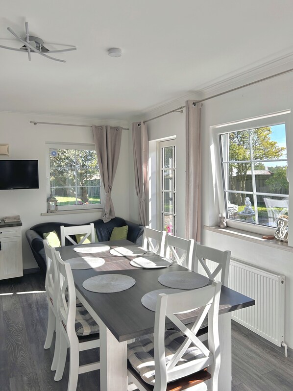 A modern dining area with a large table, white chairs, and a ceiling fan. - Apartamenty Nexo (Nexø)