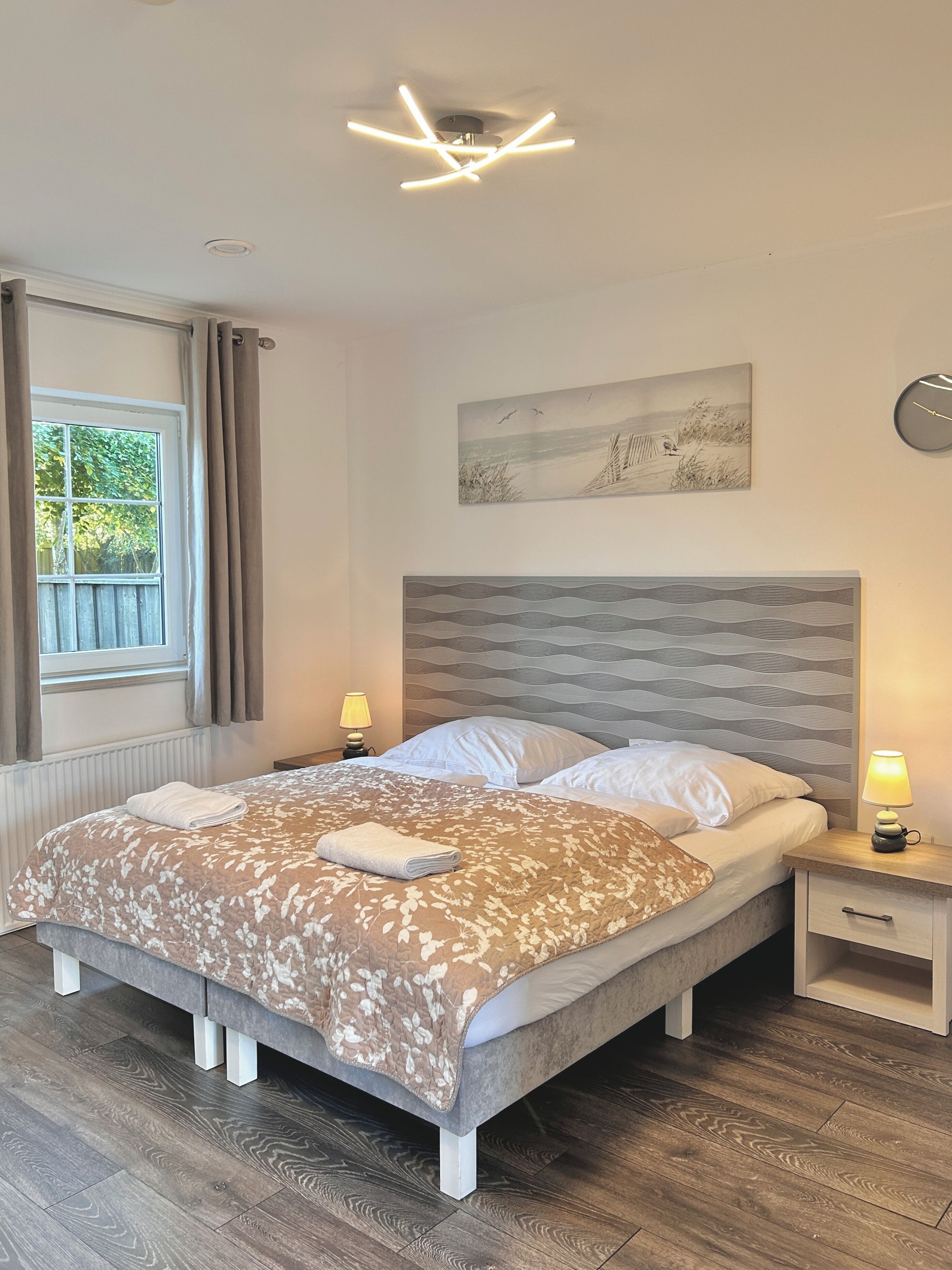 A modern bedroom with a bed, bedside tables, a ceiling fan, and a window with curtains.