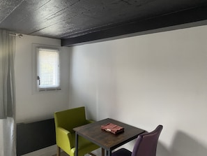 A small room with a single table and two chairs, one green and one purple. - Description en anglais (Veules-les-Roses)