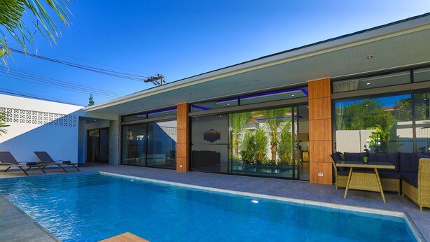 A modern pool area with a clear blue pool, lounge chairs, and a seating area with a table and chairs. - Sweet Luxury 4 Bedrooms Pool Villa (Rawai)