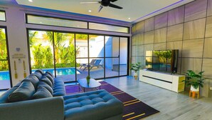A modern living room with a sofa, a TV, and a pool view. - Sweet Luxury 4 Bedrooms Pool Villa (Rawai)