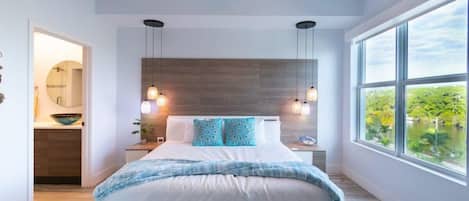 A bedroom with a bed, a ceiling fan, bedside lamps, a window with a view, and a wooden headboard.