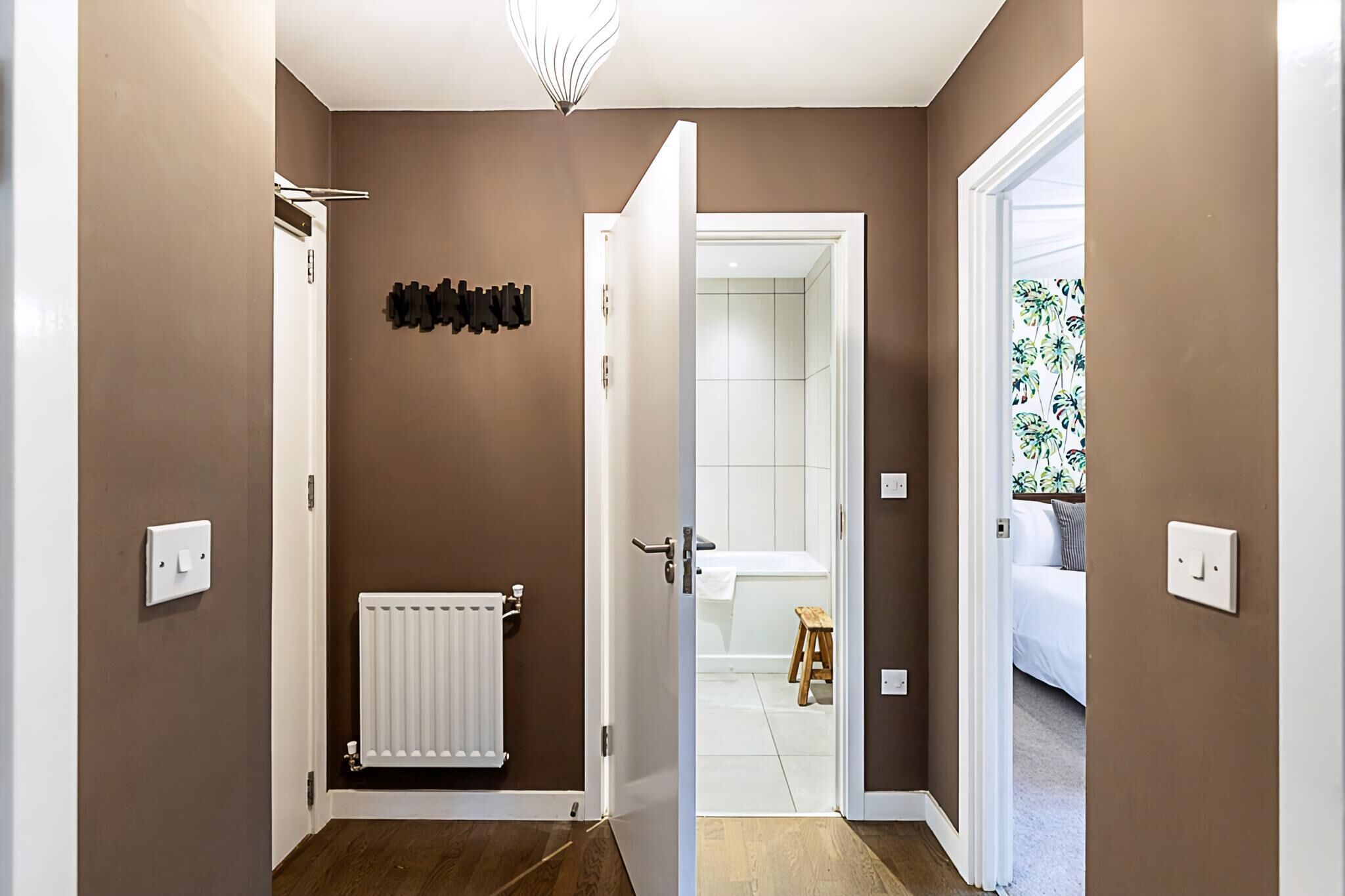 A hallway with a radiator, a coat rack, and a door leading to a bathroom.