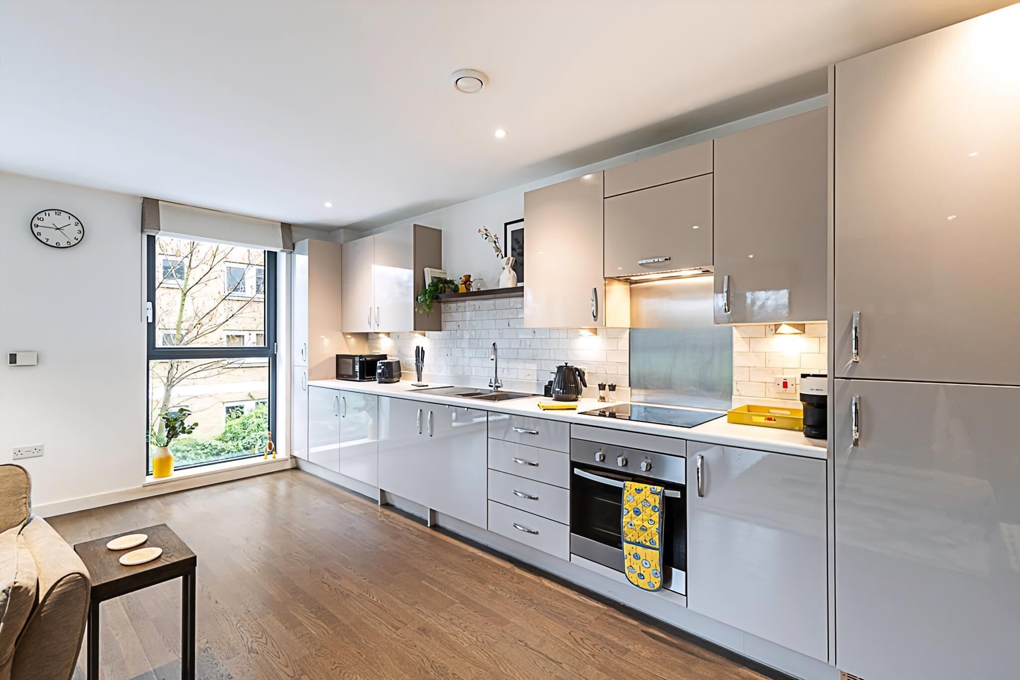 A modern kitchen with white cabinets, a large window, and a dining area with a table and chairs.