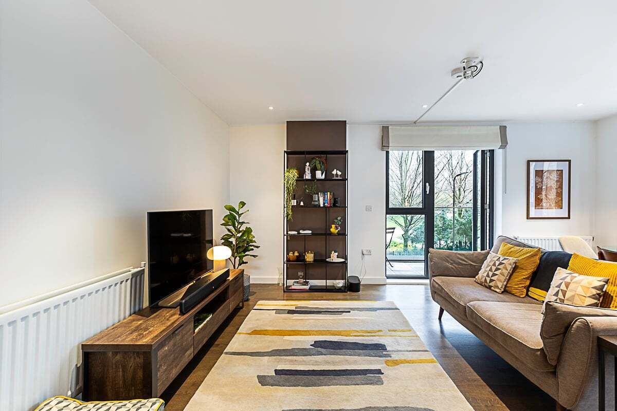 Una sala de estar moderna con un televisor de pantalla plana, una estantería, un sofá con cojines y un ventanal grande.