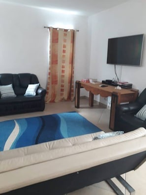 Uma sala de estar com sofá, mesa de centro, televisão e cama.