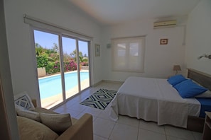 A bedroom with a bed, a chair, a window with a view of a pool, and an air conditioning unit.