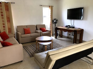 Uma sala de estar com sofá, mesa de centro, televisão e ventoinha.