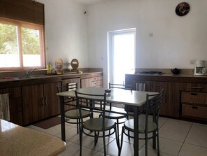 Uma cozinha com mesa de jantar, cadeiras, pia e fogão.