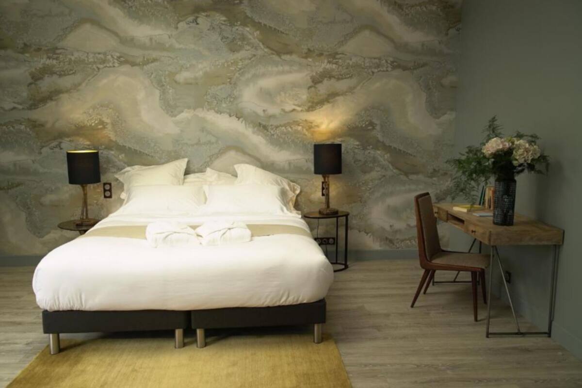 A bedroom with a large bed, two bedside tables with lamps, a wooden desk, and a chair.