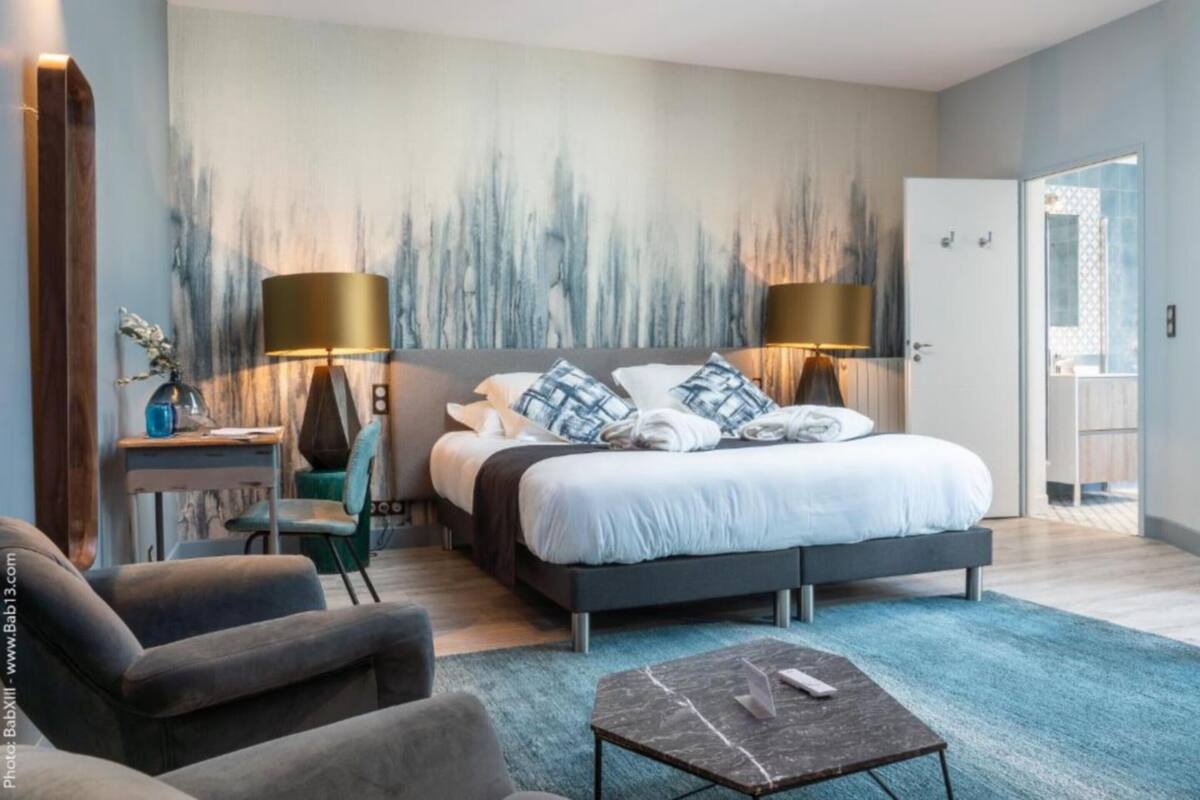 A modern bedroom with a large bed, two bedside lamps, a desk, and a chair.