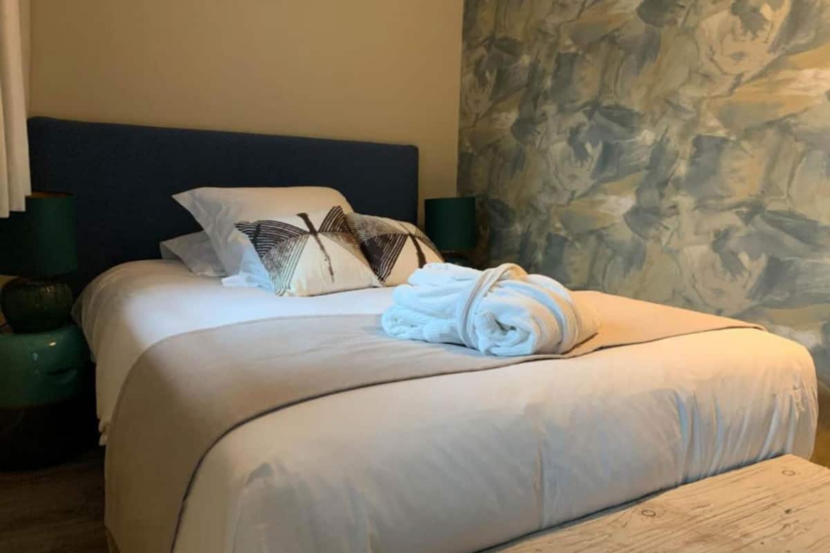 A neatly made bed with a folded towel, two pillows, and two green bedside tables with lamps.
