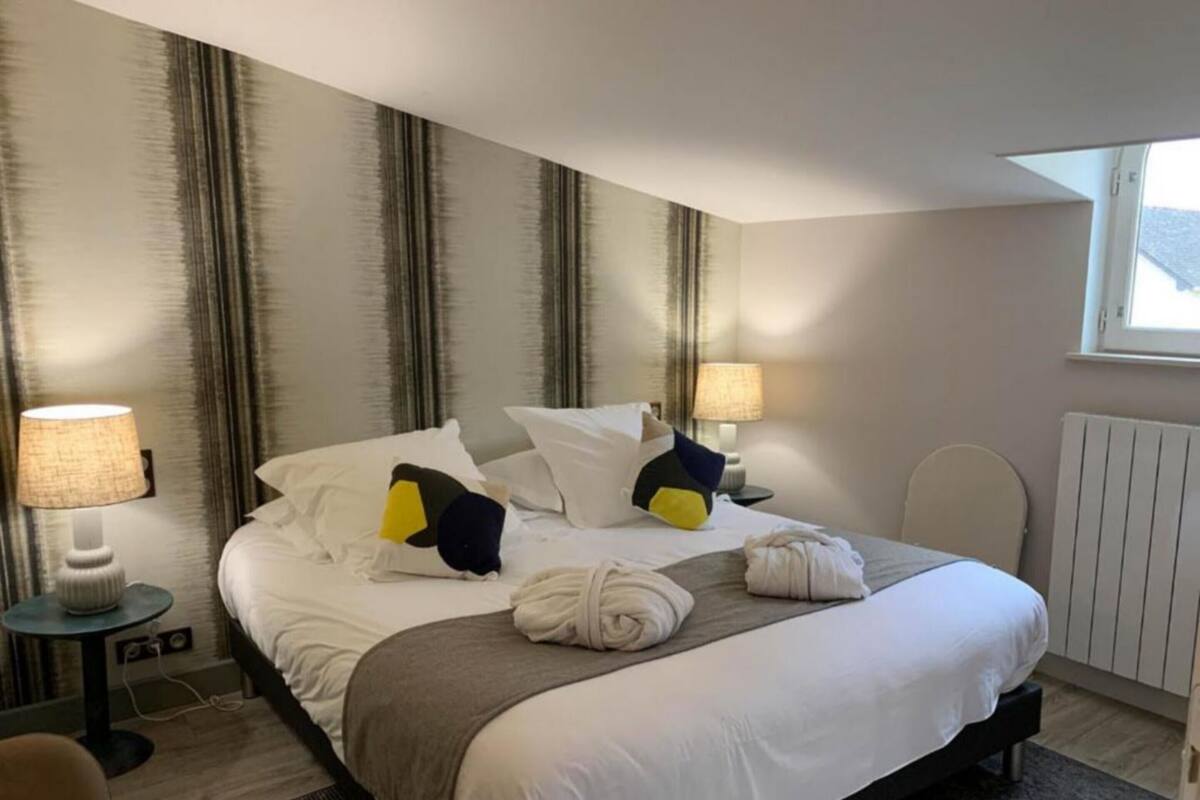 A hotel room with a bed, two bedside tables, a chair, a window, and a radiator.